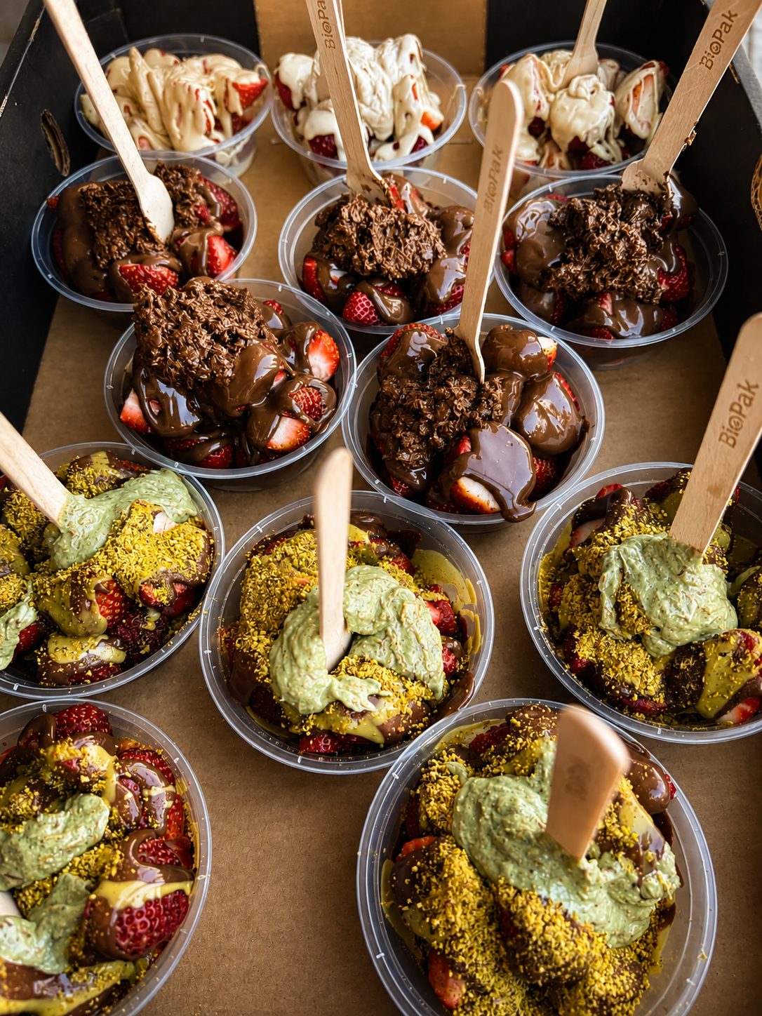 A tray of strawberry cups topped with white chocolate, milk chocolate and pistachio